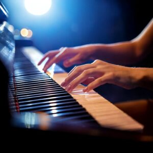 A womans hands on the keys of a piano lit by stage lighting