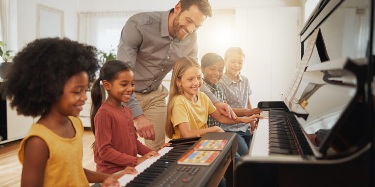 a piano teacher with several piano student children in a piano lesson